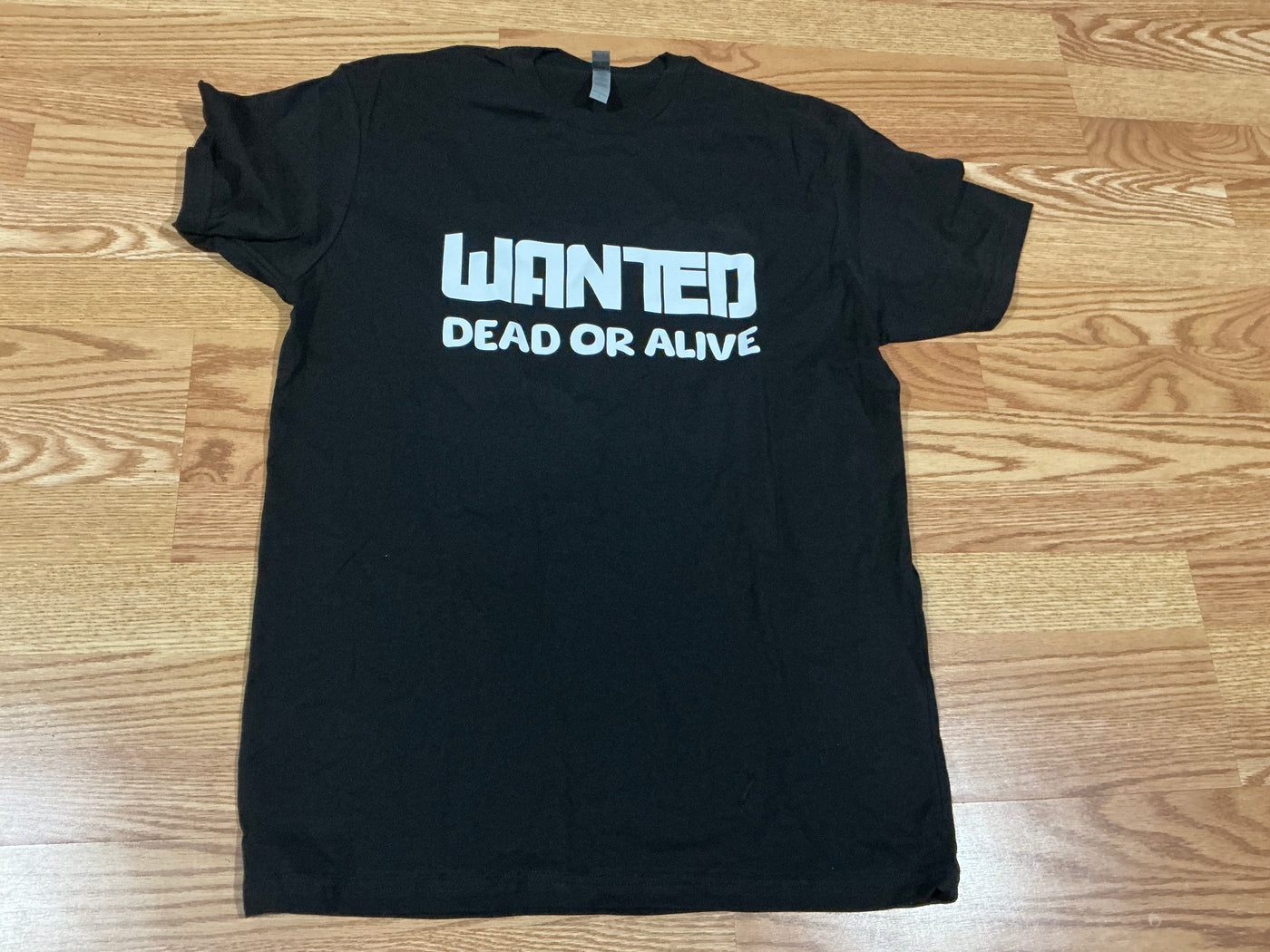 Black t-shirt with 'WANTED DEAD OR ALIVE' text on a wooden surface